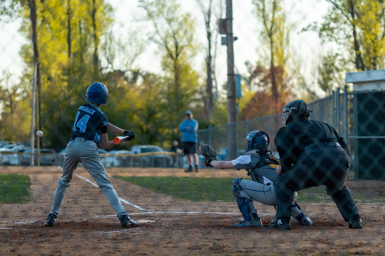 Exciting youth baseball game featuring a batter, catcher, and umpire in action at dusk.