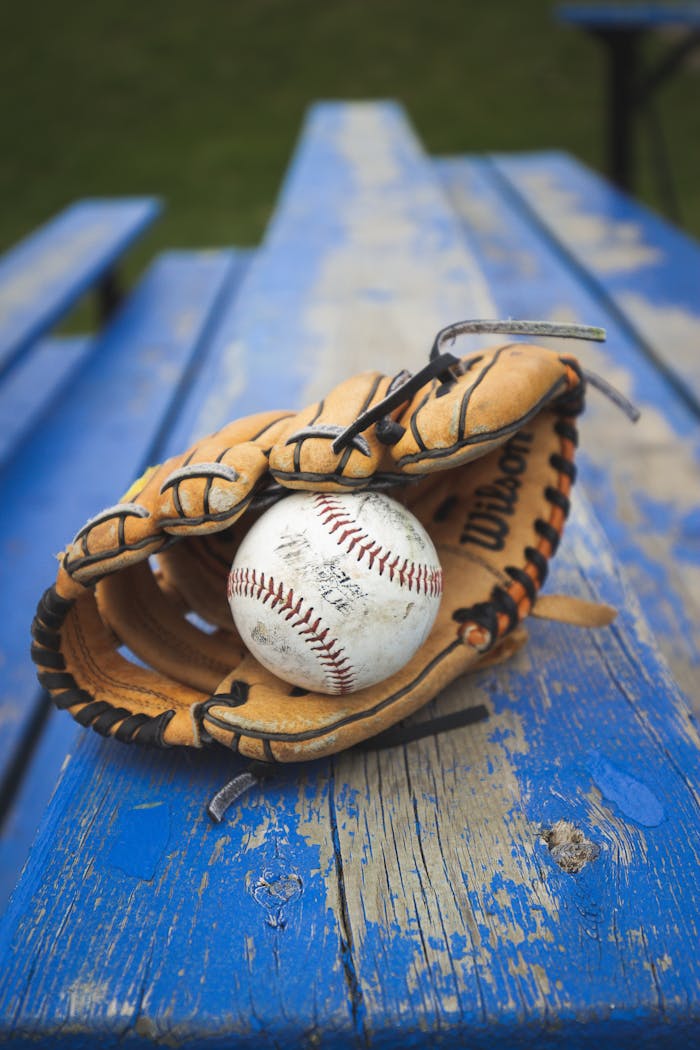 A close-up of a baseball glove holding a ball resting on a weathered blue bench outdoors.