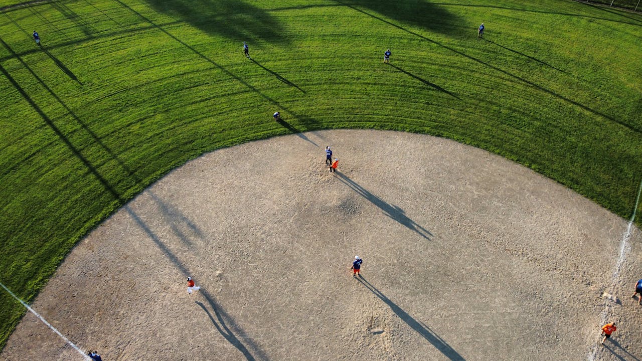 Drone shot capturing an outdoor baseball game in progress on a sunny day.